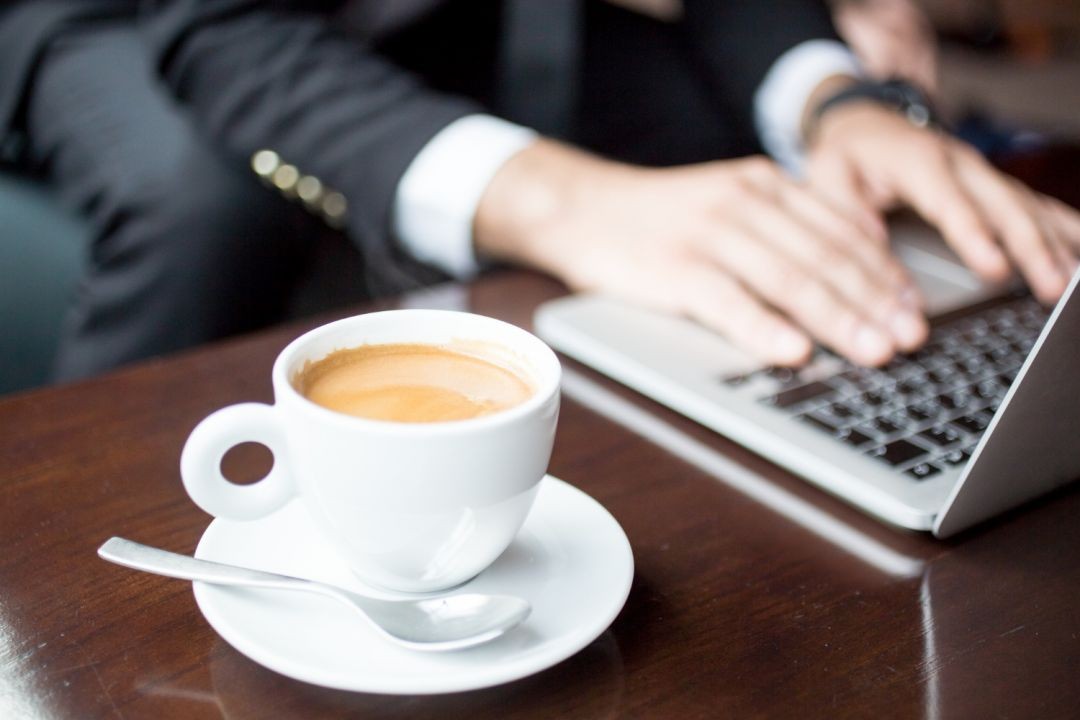 Um homem utilizando o notebook e tomando um café.